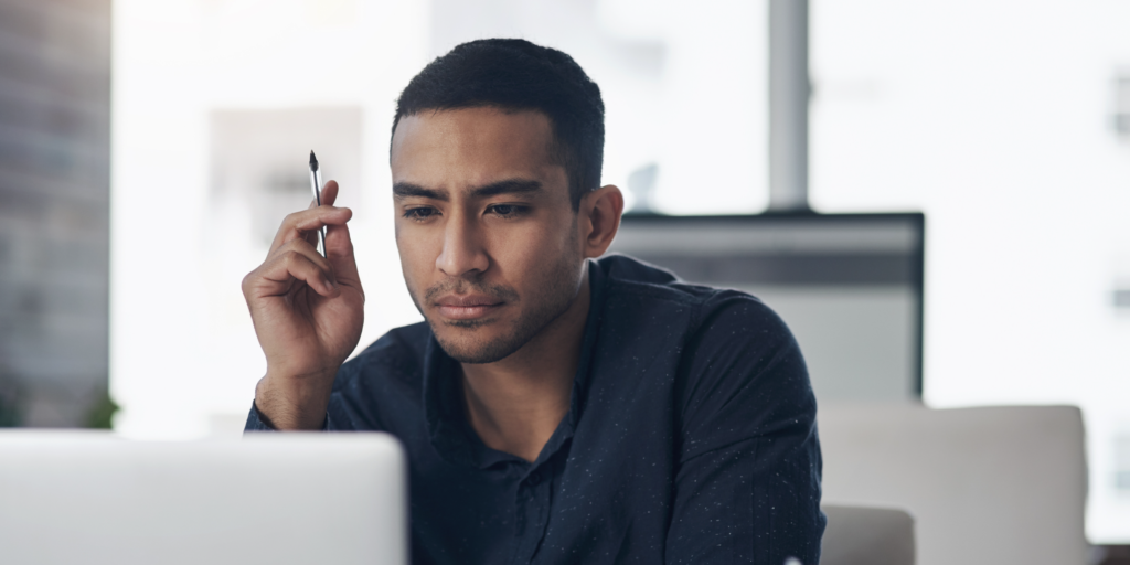 Homem negro olha para a tela de um computador com expressão reflexiva